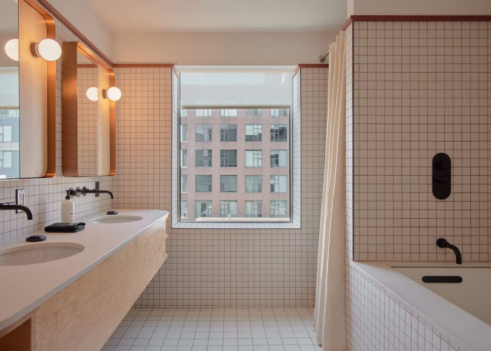 A spacious white tiled bathroom features a deep tub and two vanity areas